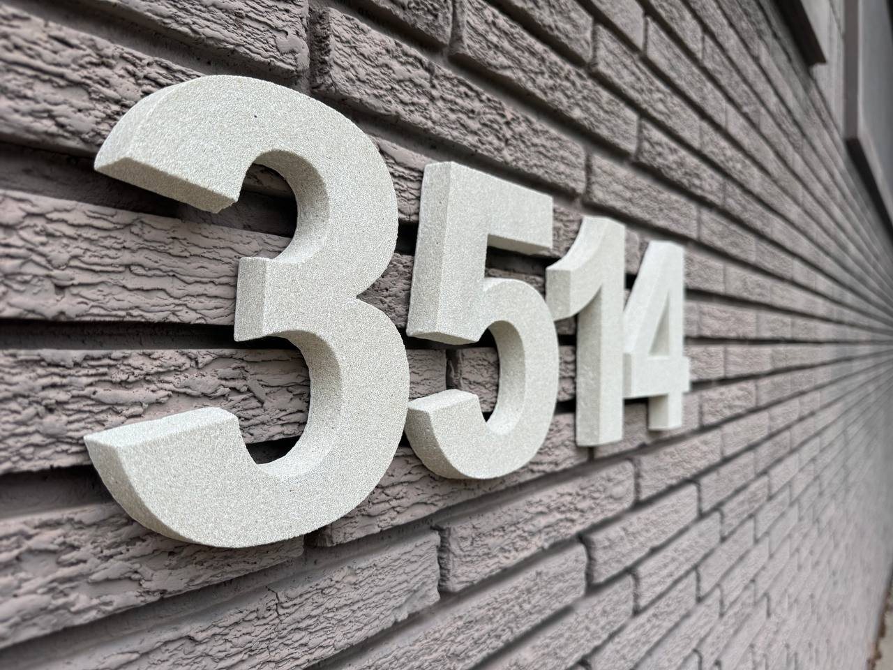 Close-up of thick raised sandstone-style house numbers on textured brick