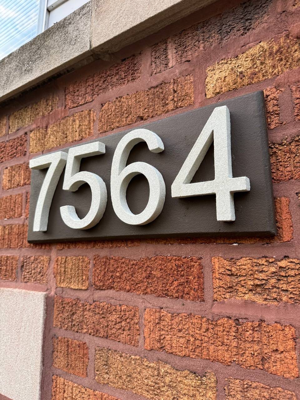 Close-up of raised stone numbers on a dark plaque mounted on red brick